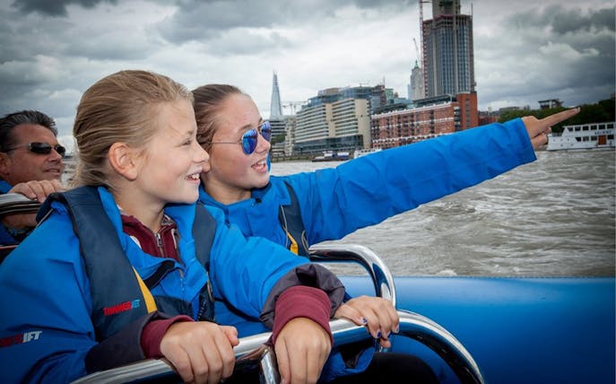 People enjoying a high-speed boat ride on the Thames River with London skyline in view.