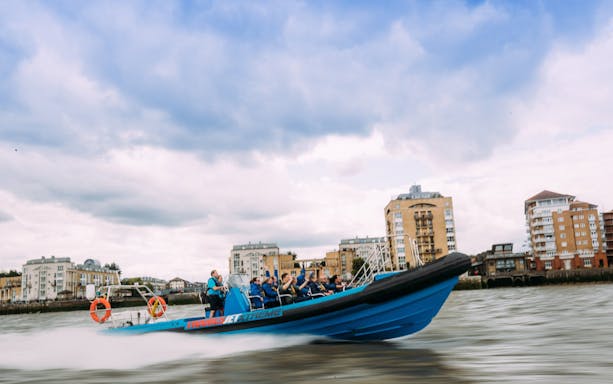 High-speed boat on the Thames River with passengers enjoying the ride, London cityscape in background.