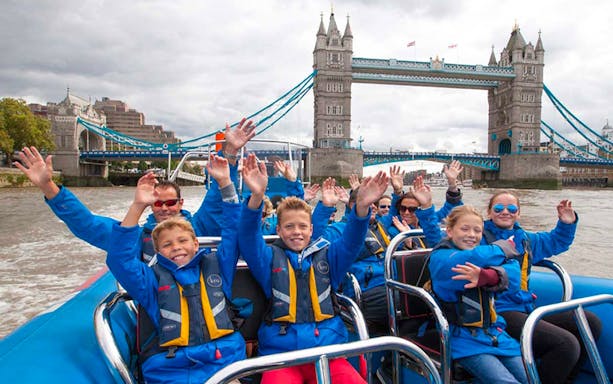 Group enjoying high-speed boat ride on the Thames River with Tower Bridge in the background, London.