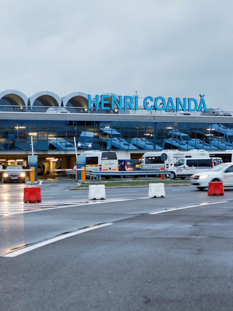 Henri Coandă Airport exterior with cars and buses in Bucharest.