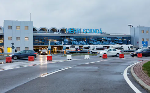 Henri Coandă Airport exterior with cars and buses in Bucharest.
