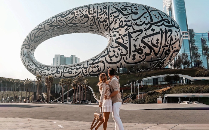 Couple admiring the Museum of the Future in Dubai with Arabic calligraphy facade.