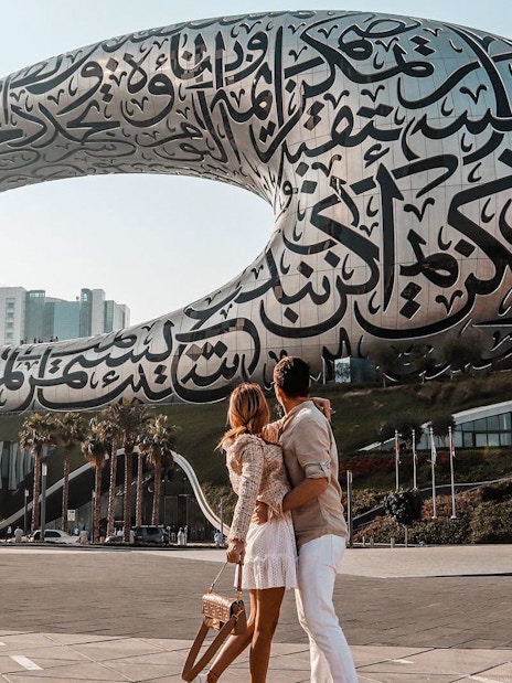 Couple admiring the Museum of the Future in Dubai with Arabic calligraphy facade.