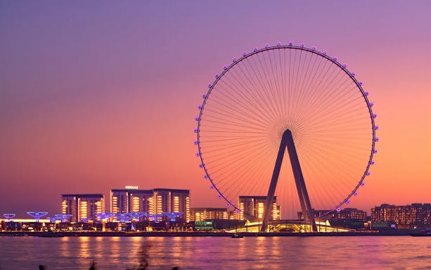 Ain Dubai Ferris wheel at sunset with city lights in the background.