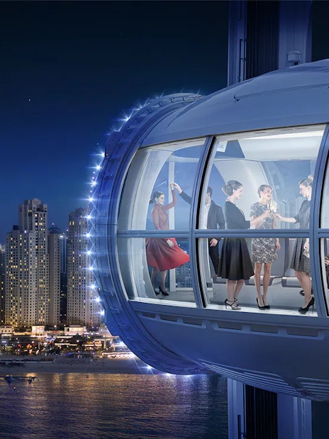 People enjoying a ride in Ain Dubai observation wheel at night, with city skyline in the background.