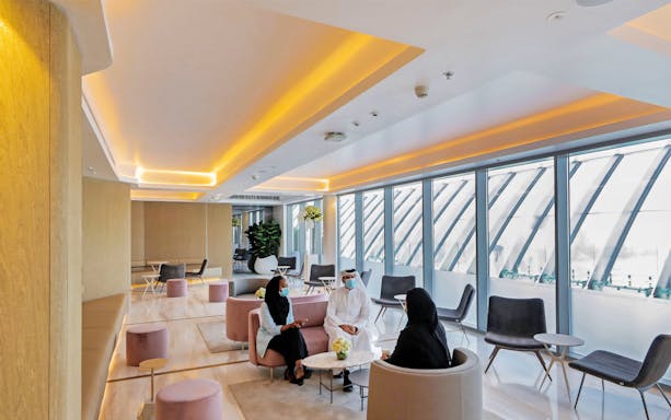 Modern lounge area at The View At The Palm, Dubai, with people seated and large windows.