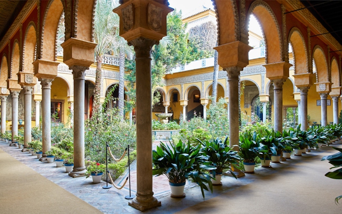 Palacio de las Dueñas courtyard with arches and lush garden in Seville.