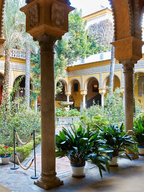 Palacio de las Dueñas courtyard with arches and lush garden in Seville.