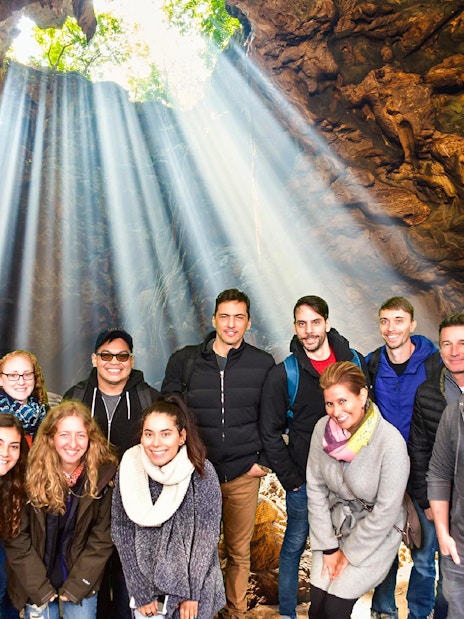 Group exploring Waitomo Glowworm Caves with light streaming through cave opening, Auckland tour.