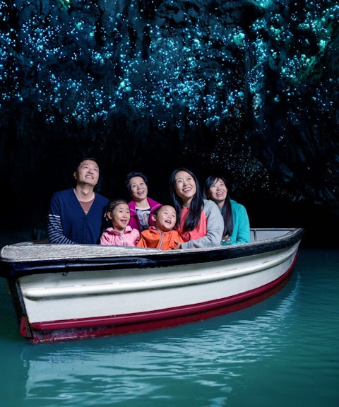 Group enjoying boat tour in Waitomo Glowworm Caves, New Zealand, with glowing ceiling.