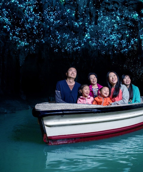 Group enjoying boat tour in Waitomo Glowworm Caves, New Zealand, with glowing ceiling.