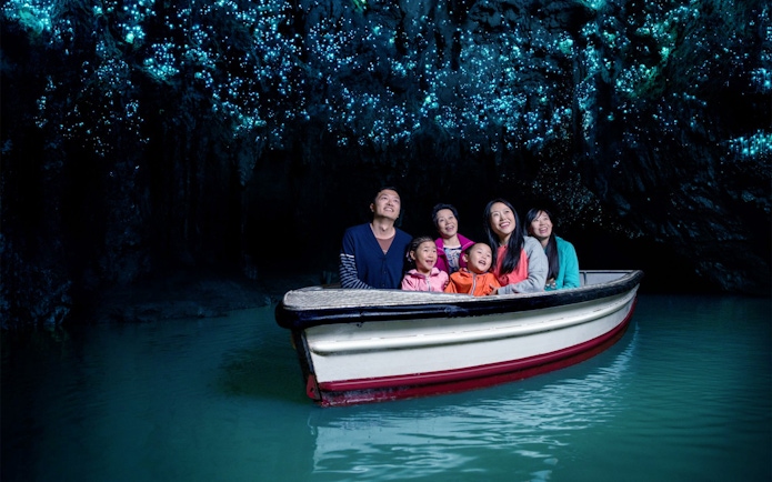 Group enjoying boat tour in Waitomo Glowworm Caves, New Zealand, with glowing ceiling.