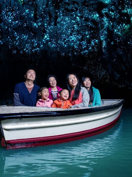 Group enjoying boat tour in Waitomo Glowworm Caves, New Zealand, with glowing ceiling.