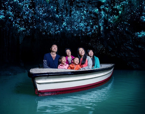 Group enjoying boat tour in Waitomo Glowworm Caves, New Zealand, with glowing ceiling.