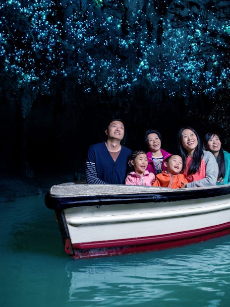 Group enjoying boat tour in Waitomo Glowworm Caves, New Zealand, with glowing ceiling.