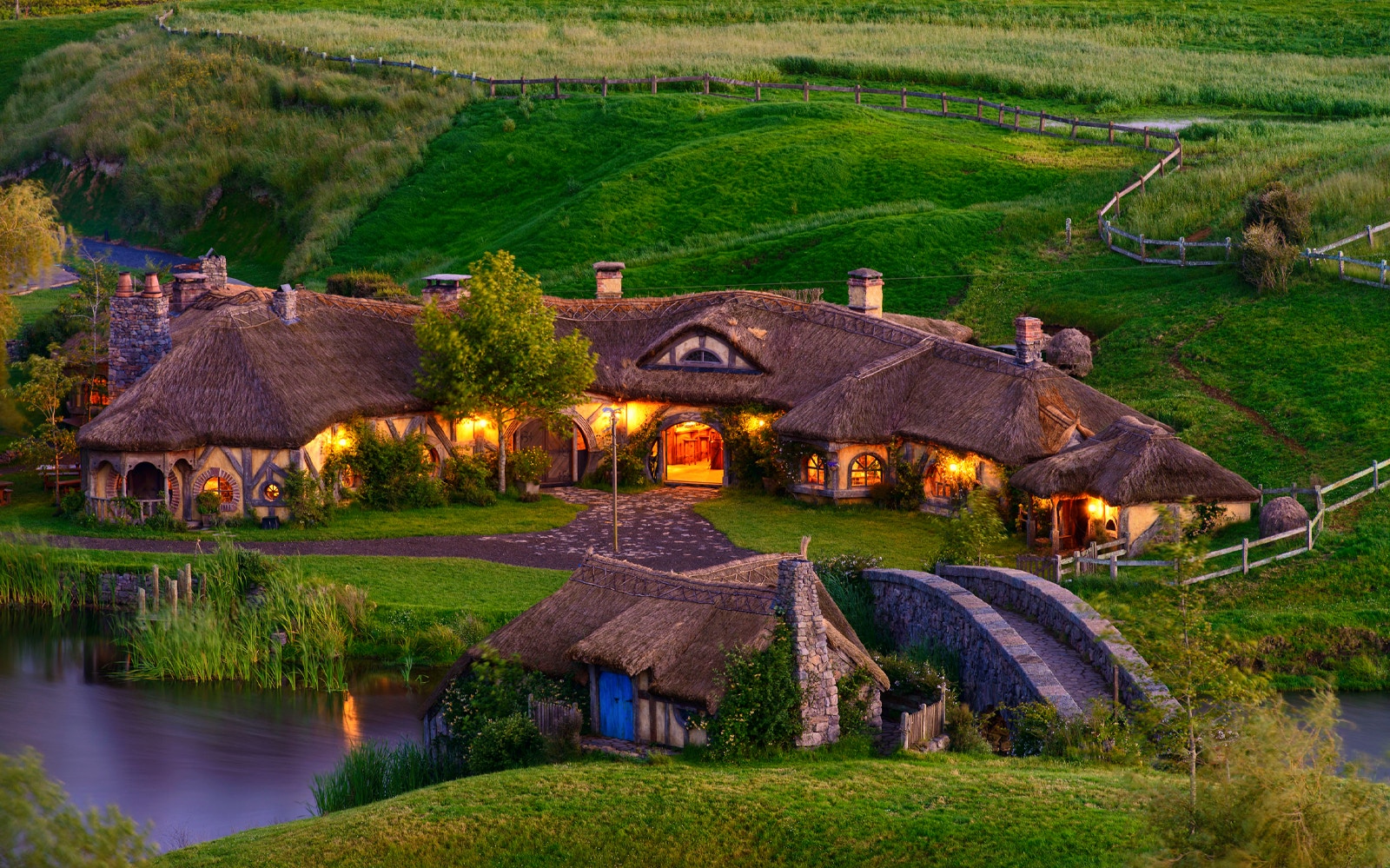Hobbiton Movie Set with illuminated hobbit houses and lush green landscape in New Zealand.