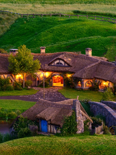 Hobbiton Movie Set with illuminated hobbit houses and lush green landscape in New Zealand.