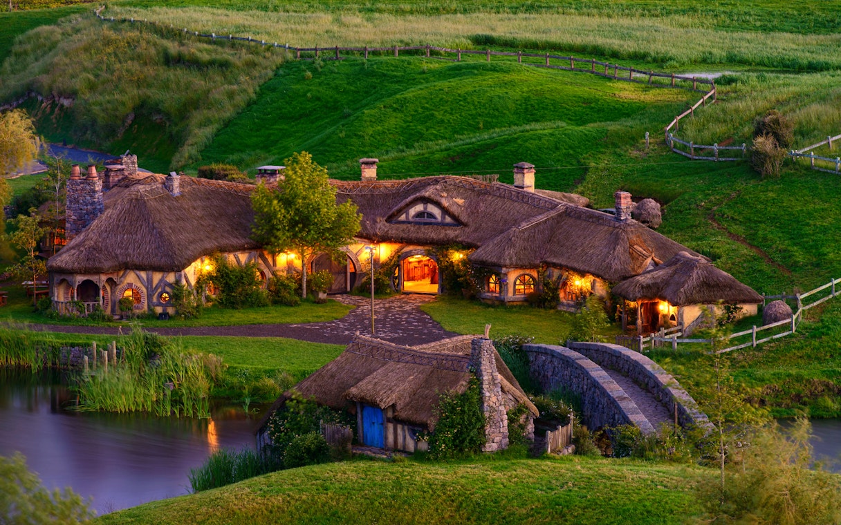 Hobbiton Movie Set with illuminated hobbit houses and lush green landscape in New Zealand.