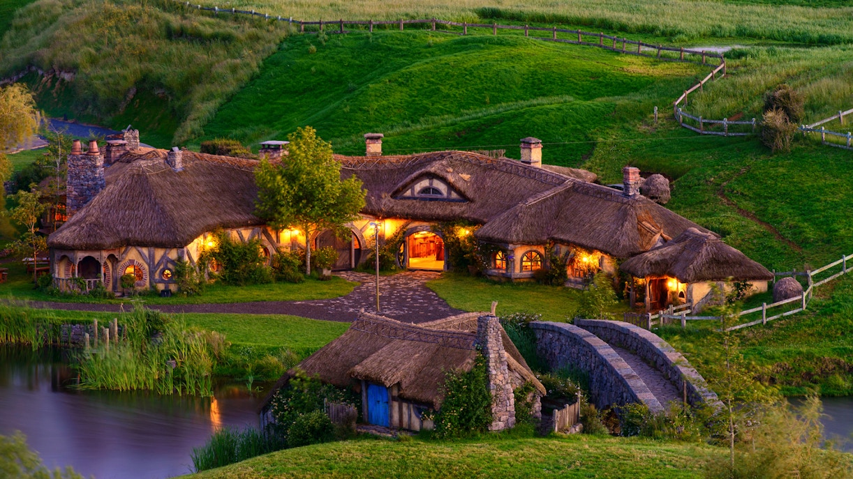 Hobbiton Movie Set with illuminated hobbit houses and lush green landscape in New Zealand.