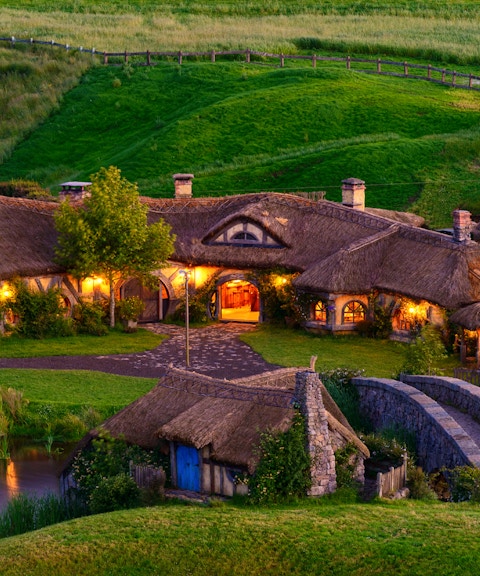 Hobbiton Movie Set with illuminated hobbit houses and lush green landscape in New Zealand.
