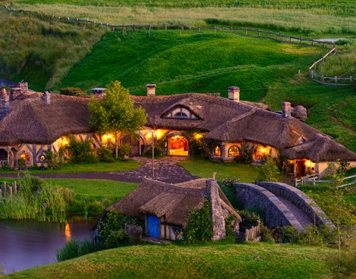 Hobbiton Movie Set with illuminated hobbit houses and lush green landscape in New Zealand.