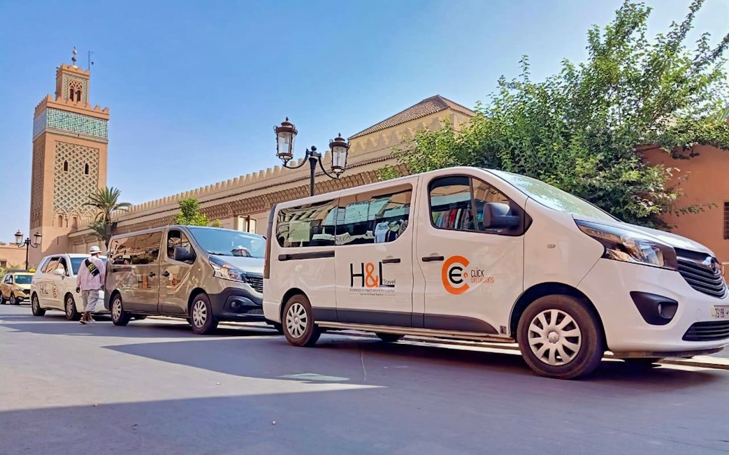 Private airport transfer vans in Marrakesh with Koutoubia Mosque in the background.