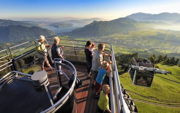 Tourists enjoying panoramic views from Mt. Stanserhorn, with cable car descending, near Zürich.