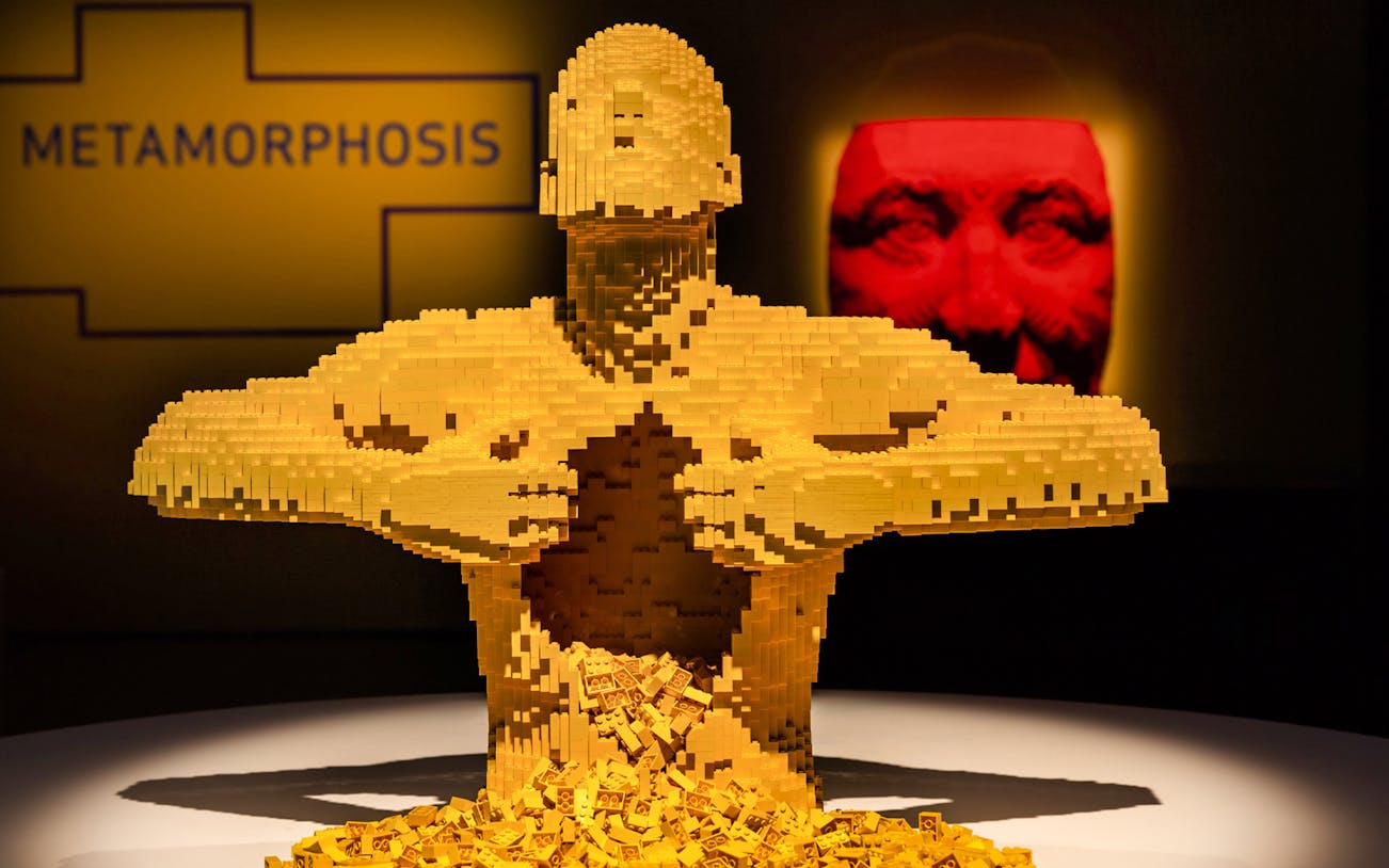 Yellow LEGO sculpture of a human figure opening its chest at The Art of the Brick exhibition.