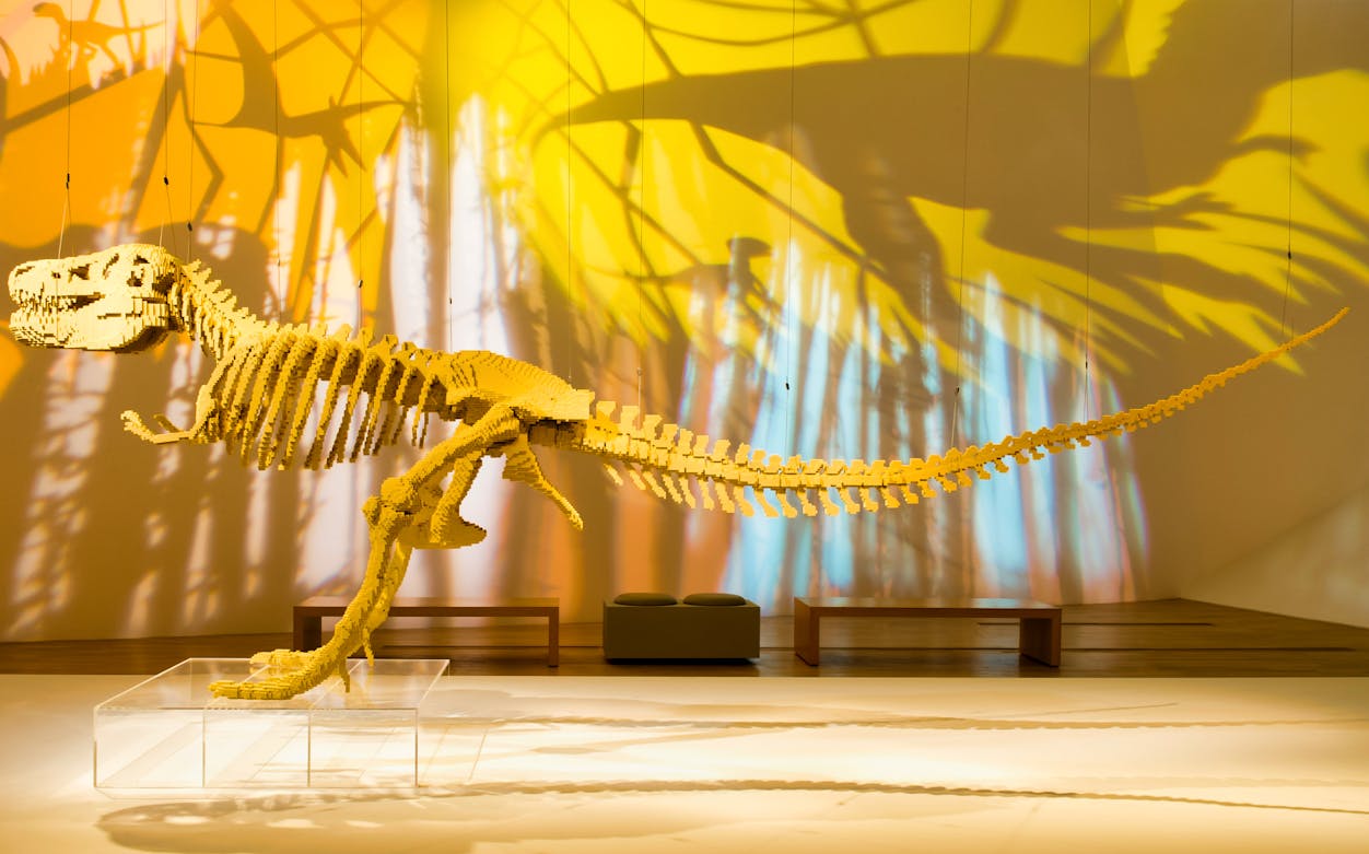 LEGO dinosaur sculpture at The Art of the Brick exhibition with colorful shadows.