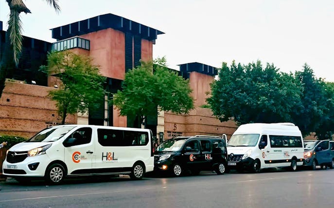 Private transfer vehicles parked outside Marrakesh building for Essaouira Airport service.