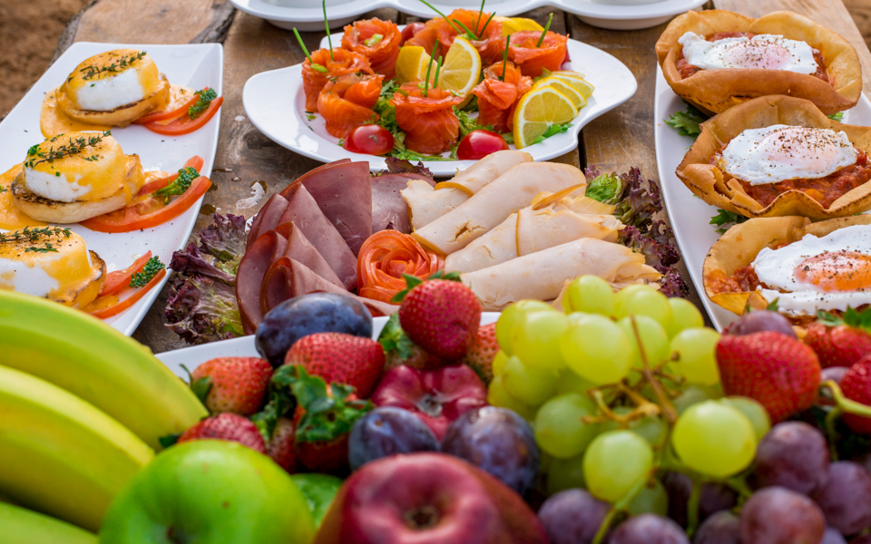 Breakfast spread with fresh fruits, eggs, and meats on a Morning Camel Safari tour.