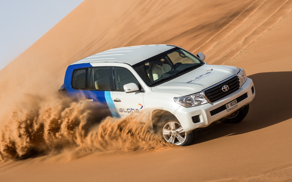SUV driving through desert dunes during morning camel safari.