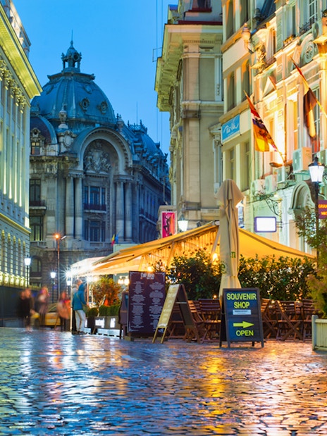 Bucharest street at night with illuminated buildings and outdoor cafes.