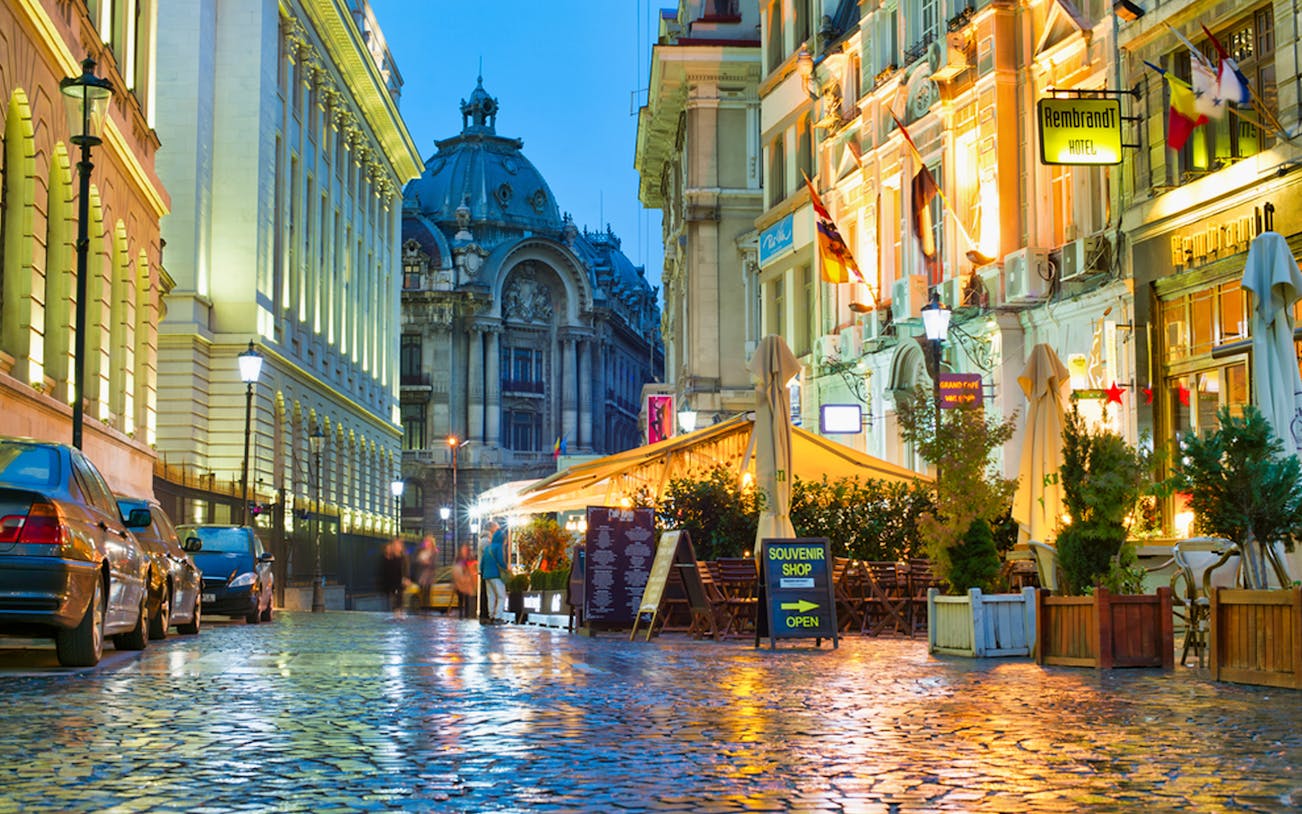 Bucharest street at night with illuminated buildings and outdoor cafes.