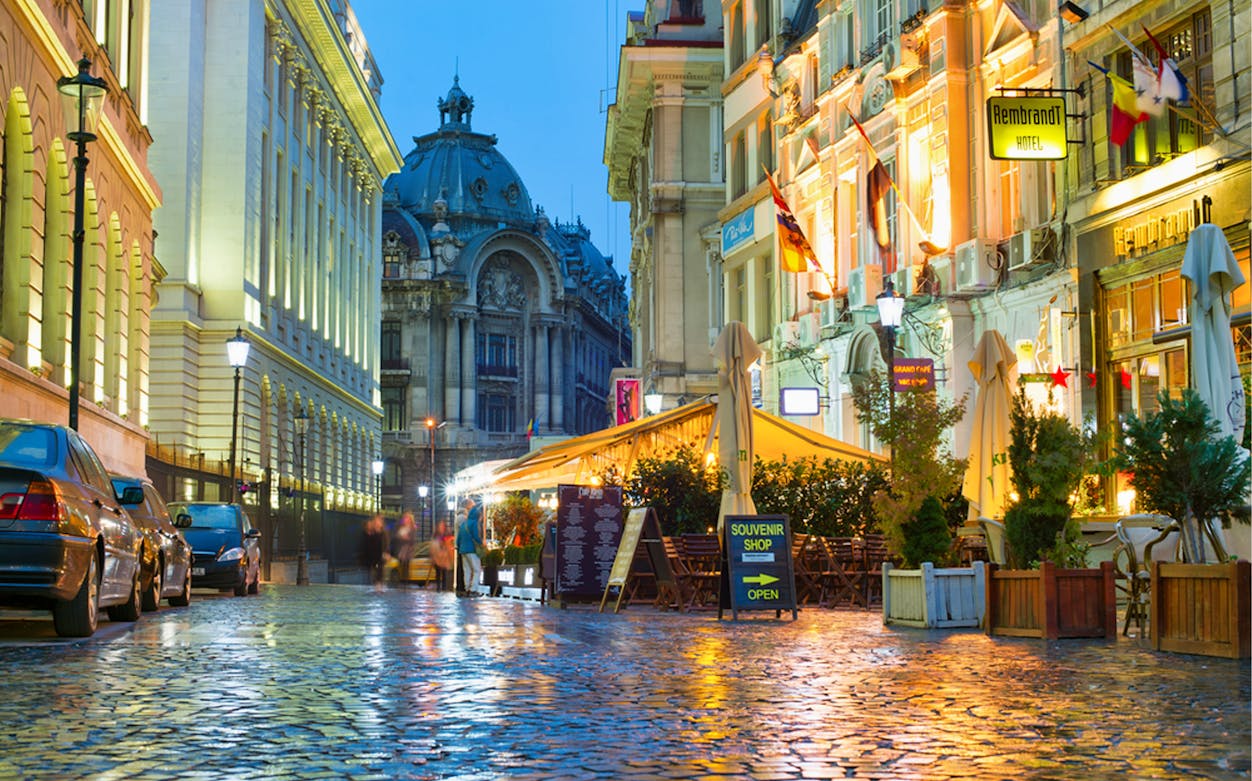 Bucharest street view with historic architecture and outdoor cafes at dusk.