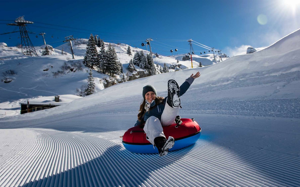 Person snow tubing on Mount Titlis with ski lifts and snowy trees in the background.