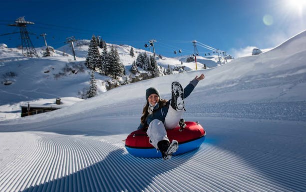 Person snow tubing on Mount Titlis with ski lifts and snowy trees in the background.