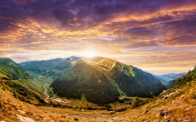 Transfagarasan mountain road at sunrise, Romania, with lush green valleys.