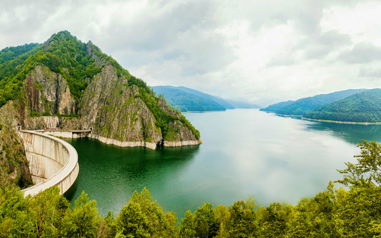 Transfagarasan road curving around Vidraru Dam with lush green mountains in Romania.
