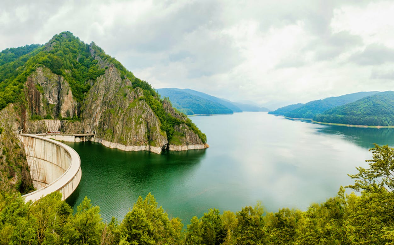 Transfagarasan road curving around Vidraru Dam with lush green mountains in Romania.