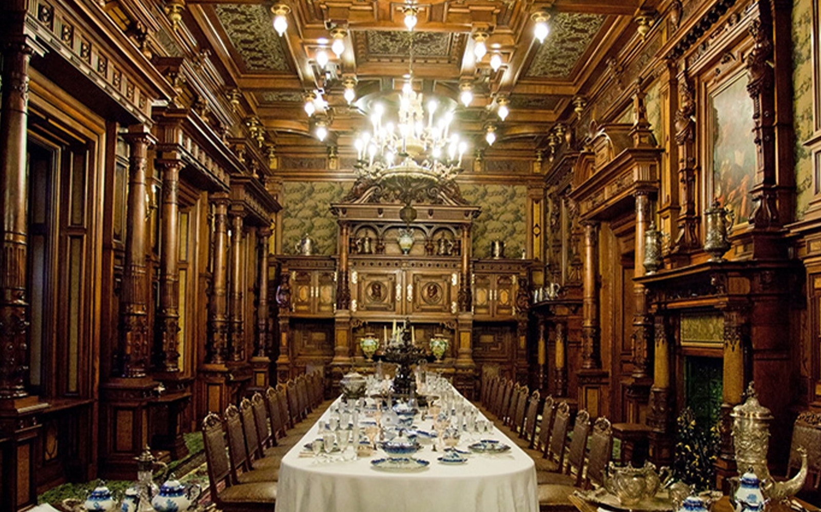 Dining room with ornate woodwork and long table set for a banquet at Peles Castle, Romania.