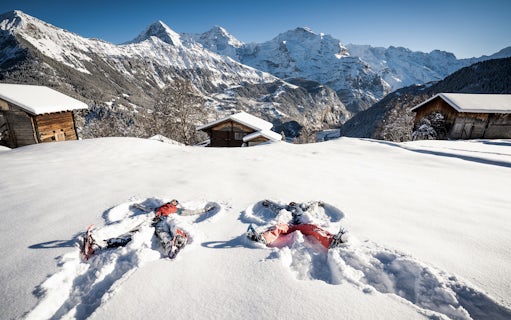 Snowshoers making snow angels in the Swiss Alps with wooden cabins and mountains in the background.