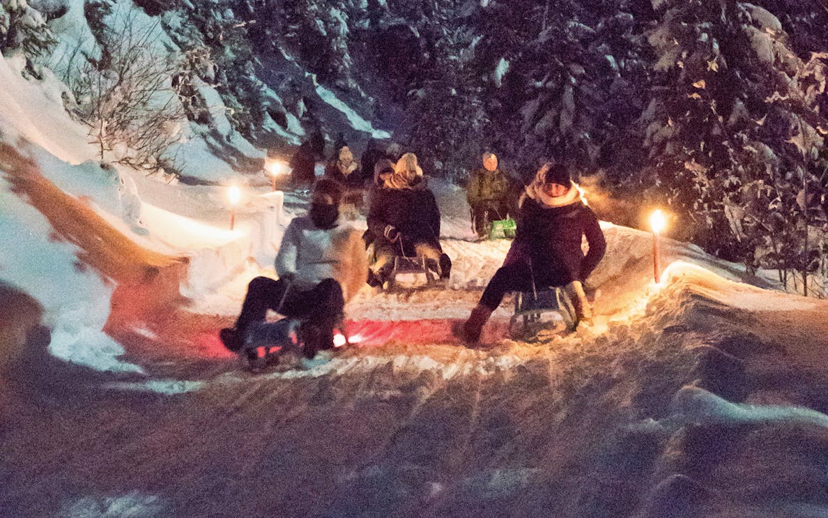 Night sledding on a snowy trail with torches, part of a tour with optional cheese fondue dinner.
