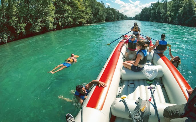 People rafting on the Aare River from Thun to Bern, with one person swimming nearby.