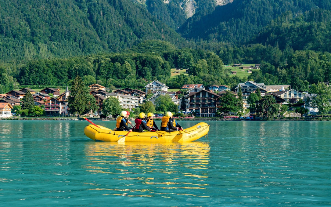 Family rafting on Lake Brienz with scenic mountain and village backdrop.