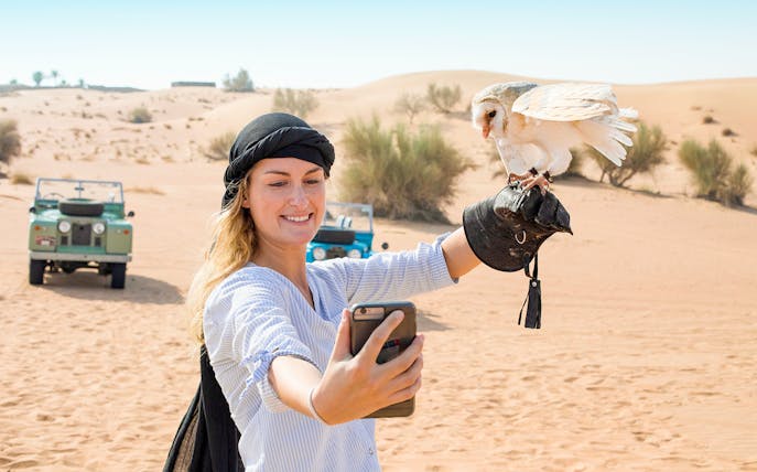 Selfie with owl during Bedouin safari in desert, vintage jeep in background.