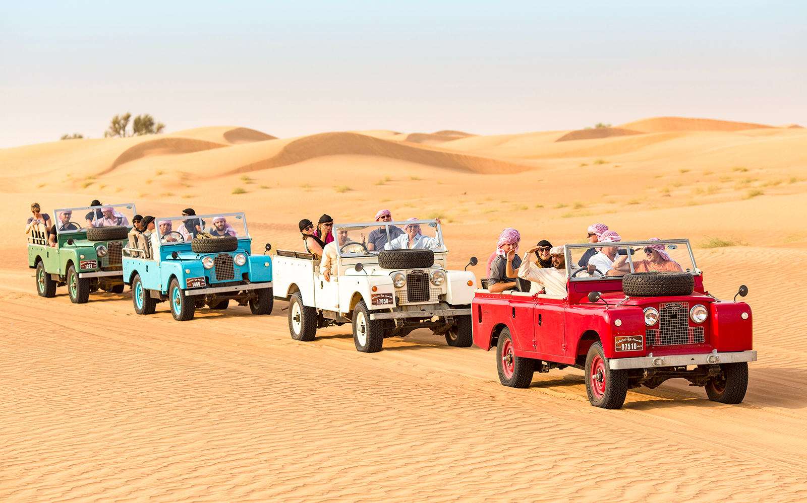 Vintage Land Rovers driving through desert dunes on a Premium Heritage Safari.