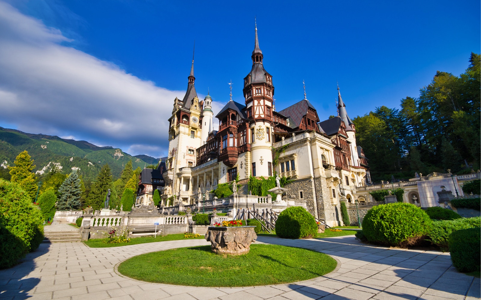 Peles Castle in Sinaia, Romania, with gardens and mountain backdrop.