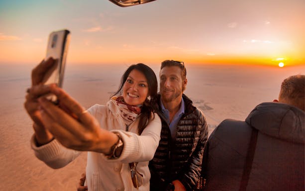 Couple taking a selfie during a hot air balloon ride at sunrise over the desert.
