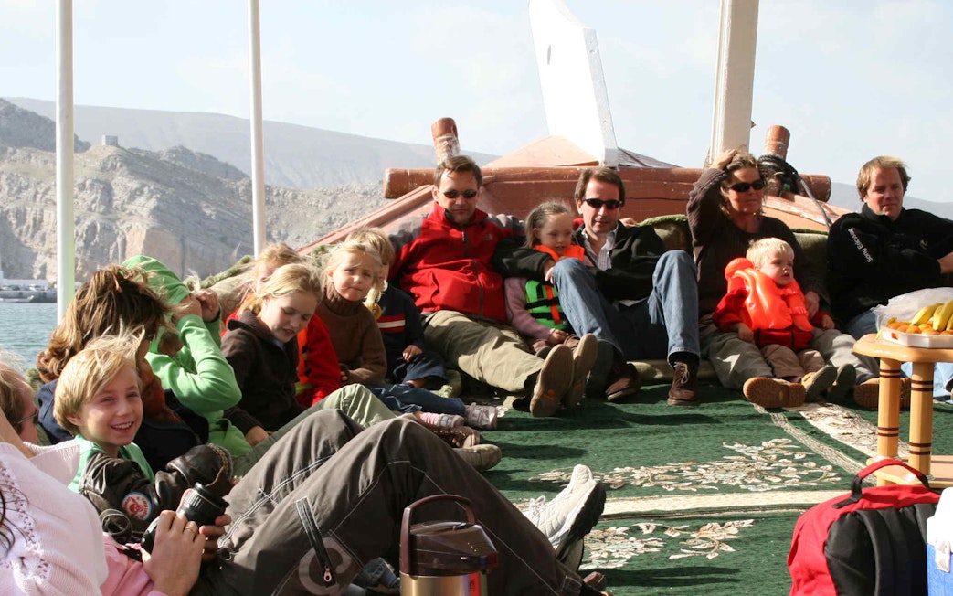 Group of people relaxing on a dhow cruise during Musandam Dibba tour with mountains in the background.